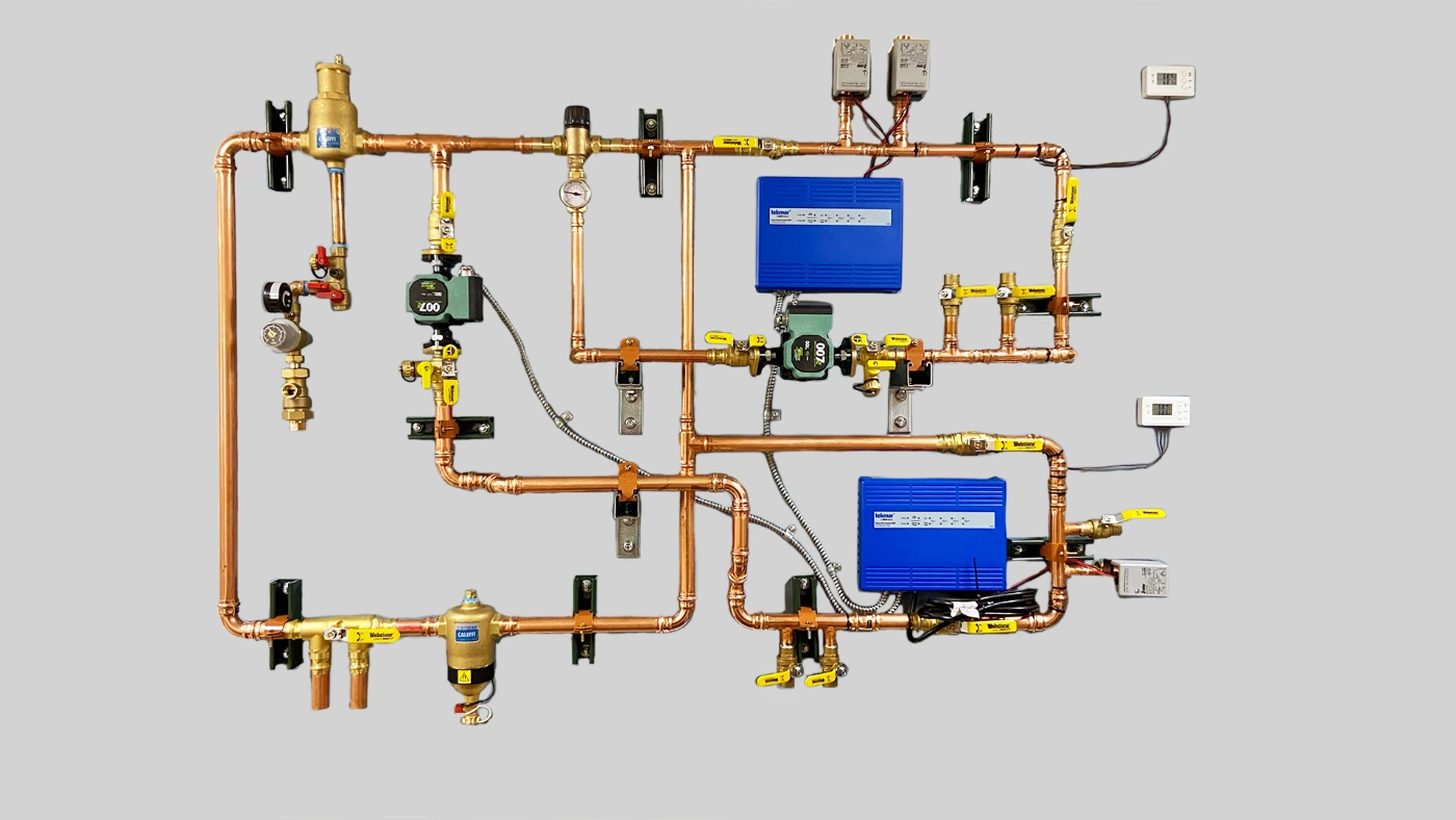 A completed pre-piped boiler board: air separator, fill valve and backflow preventer, two circulator pumps, isolation valves, zone valve actuators, controls, headers and a magnetic dirt separator, all made up on one mounting board
