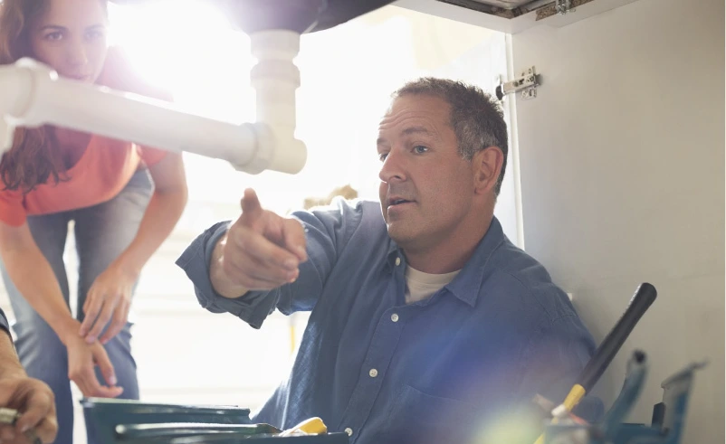 A contractor talking a homeowner through the pipework under a fitting, pointing out how the connections run