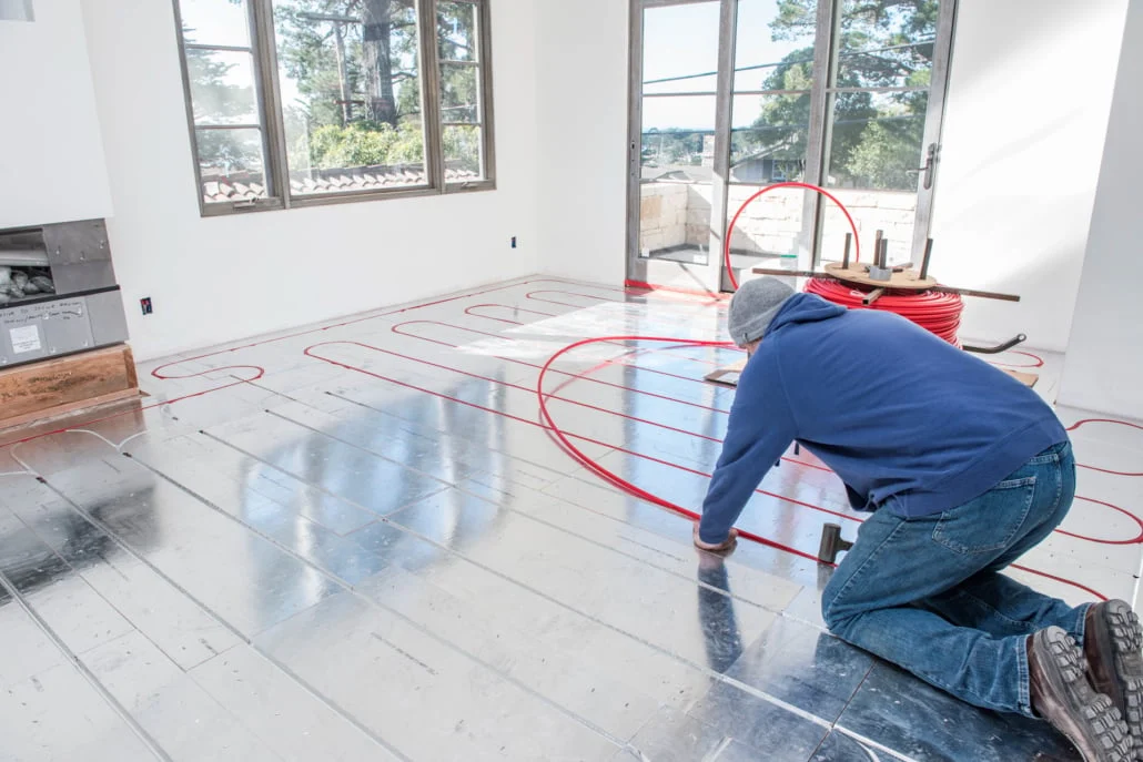 An installer kneeling on a floor of Ecowarm panels, pressing PEX tubing down into the grooves