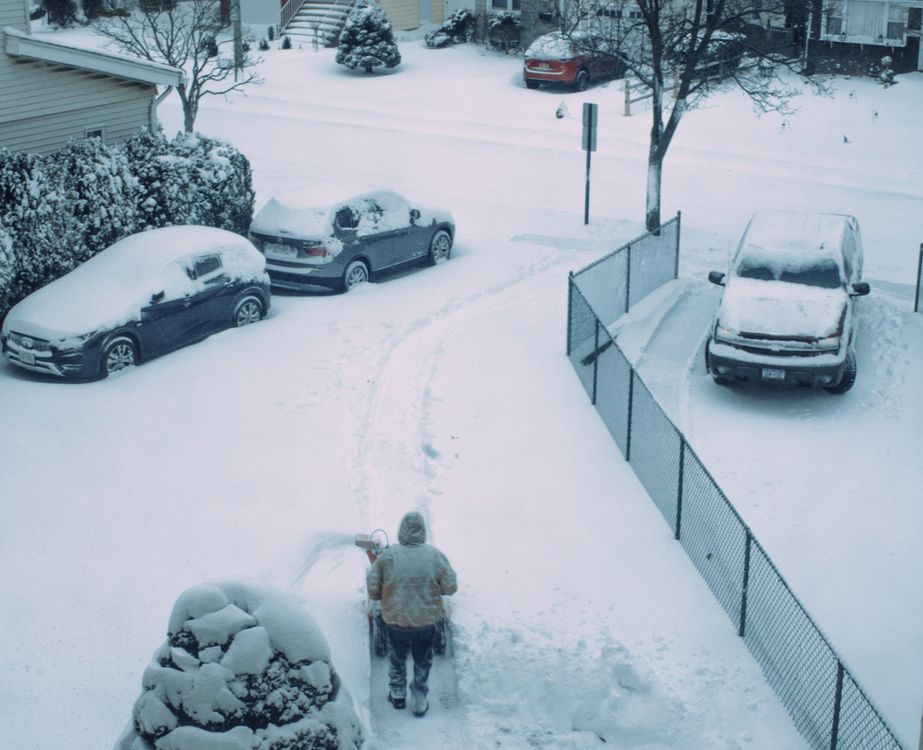 Person shoveling snow from driveway in winter - the problem a heated hydronic driveway eliminates